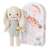 A knitted bunny plush toy, Cuddle + Kind Tiny Henry The Bunny, wearing a light green romper with a tiny carrot in the pocket, stands next to an illustrated cardboard box featuring mushrooms, flowers, and the text "Henry the Bunny." The handmade doll is made from 100% cotton and comes packaged in a whimsically designed box.