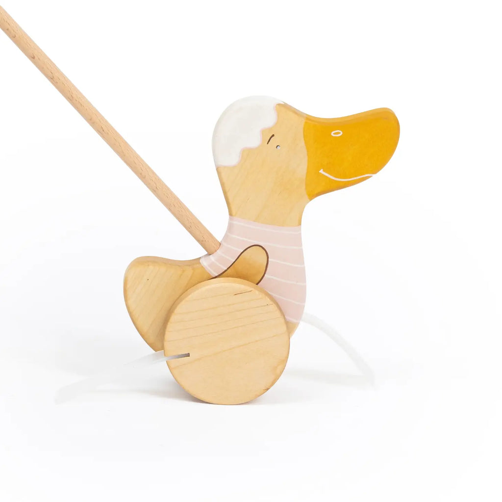 Introducing the Handmade Wooden Duck Push Toy in Light Pink: A delightful duck on wheels, made from sustainably sourced birch wood. It features a cheerful face and a long stick handle, dressed in a stylish striped design. Its wheels glide effortlessly, and it's finished with natural milk paint for an enduring charm.