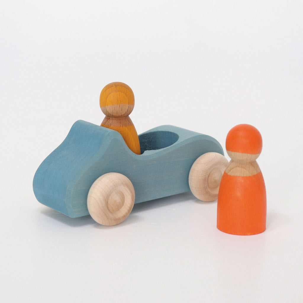 A Grimm's Wooden Blue Convertible Car with natural wooden wheels and a slot for one wooden peg figure, which is seated in the car. Another peg figure, painted orange with a non-toxic color stain, stands beside the toy car on a white background, part of the charming Rainbow Friends toy set.