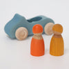 A Grimm's Wooden Blue Convertible Car with natural wood-colored wheels sits in the background. In the foreground, two Rainbow Friends peg dolls, one painted in orange and the other in yellow with non-toxic water based stain, stand side by side.