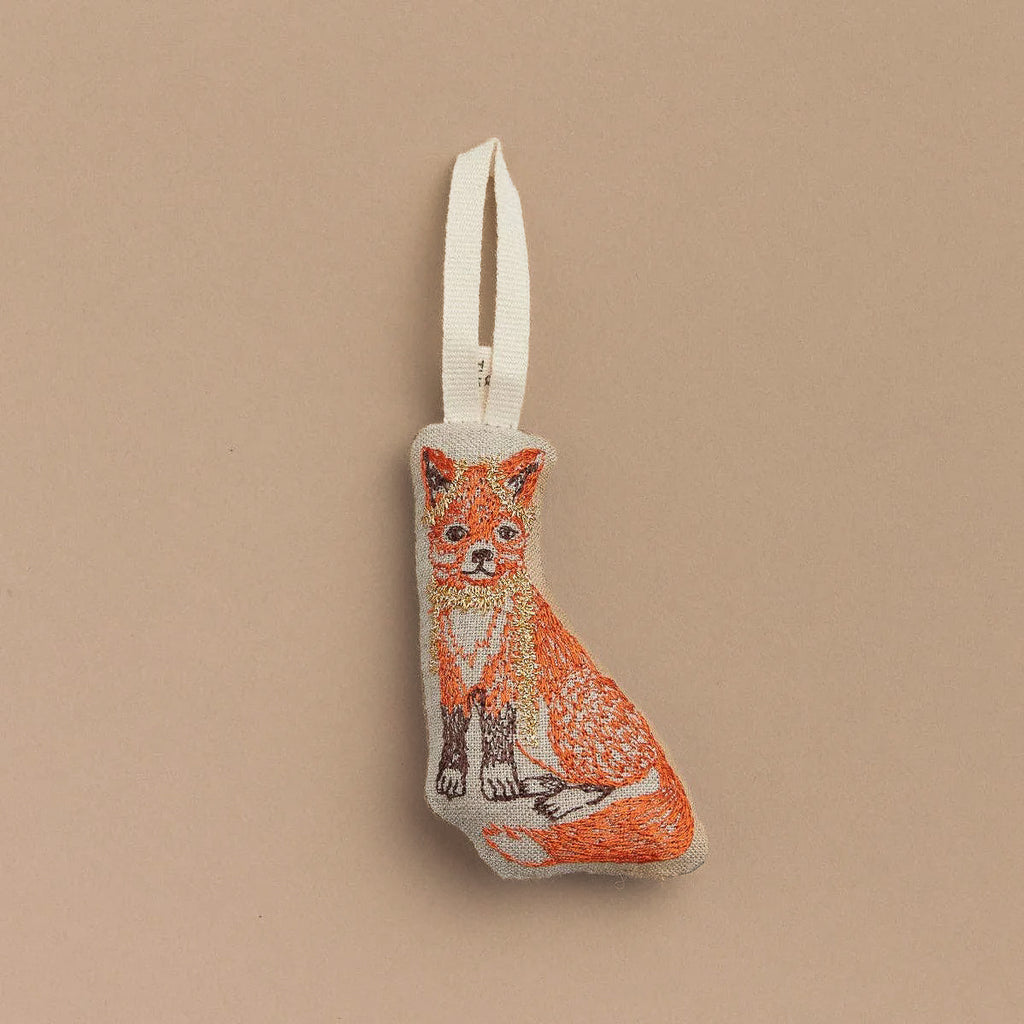 Preserve your holiday memories with the Fox Tree Trimmer Ornament. This charming ornament showcases an embroidered design of a sitting fox in vibrant orange and white hues. It comes with a convenient white hanging loop and is displayed against a simple beige background, making it an ideal Christmas gift for loved ones.