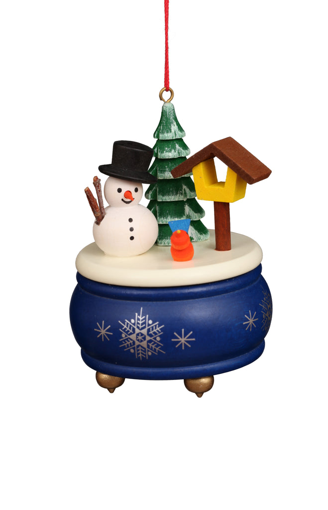 Introducing the Christian Ulbricht Ornament - Snowman: A delightful festive decoration crafted in Germany, showcasing a snowman adorned with a black hat and red scarf next to a green Christmas tree and birdhouse. Set on an elegant blue base with a snowflake pattern, this 3-inch music box serves as an ideal decorative piece, although it is not intended as a toy.