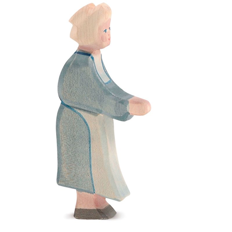 The Ostheimer Grandmother is a handcrafted wooden figurine with light-colored hair, dressed in a blue robe and white apron. The figure stands upright with slightly bent arms and legs, depicted from the side. As with all Ostheimer toys, the details are minimalistic and painted in muted colors to inspire imaginative play.