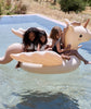 Three smiling children of diverse backgrounds enjoy a sunny day in a pool, riding together on a large Inflatable Unicorn Float.