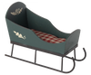 The Maileg Christmas Sleigh - Green is a charming small decorative sleigh adorned with white floral designs on its sides and a red and white checkered cushion inside. It is supported by metal runners, showcasing hand-painted details that lend it a classic, rustic look.