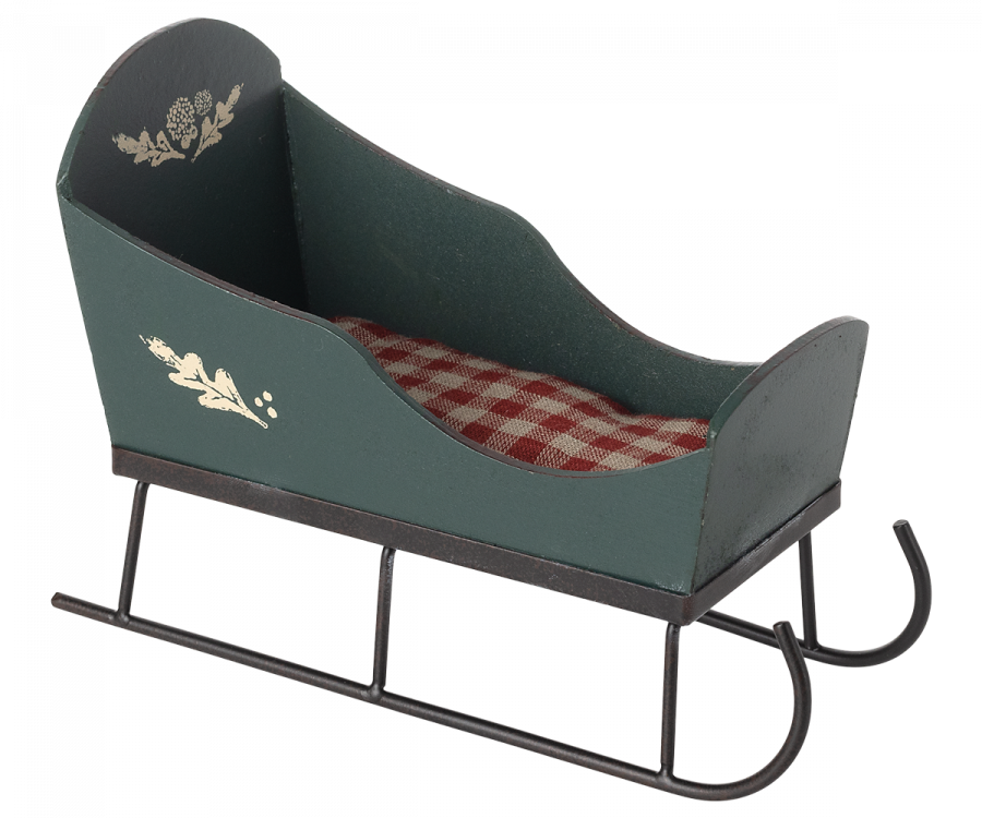 The Maileg Christmas Sleigh - Green is a charming small decorative sleigh adorned with white floral designs on its sides and a red and white checkered cushion inside. It is supported by metal runners, showcasing hand-painted details that lend it a classic, rustic look.