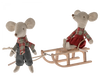 Two fabric mice dolls, both dressed in plaid shirts and scarves, bring winter charm. One mouse, wearing pants, pulls a Maileg Christmas Mini Sled with a rope. The other mouse, in a red skirt, sits on the sled enjoying the ride—a delightful snow toy and winter accessory combined beautifully.