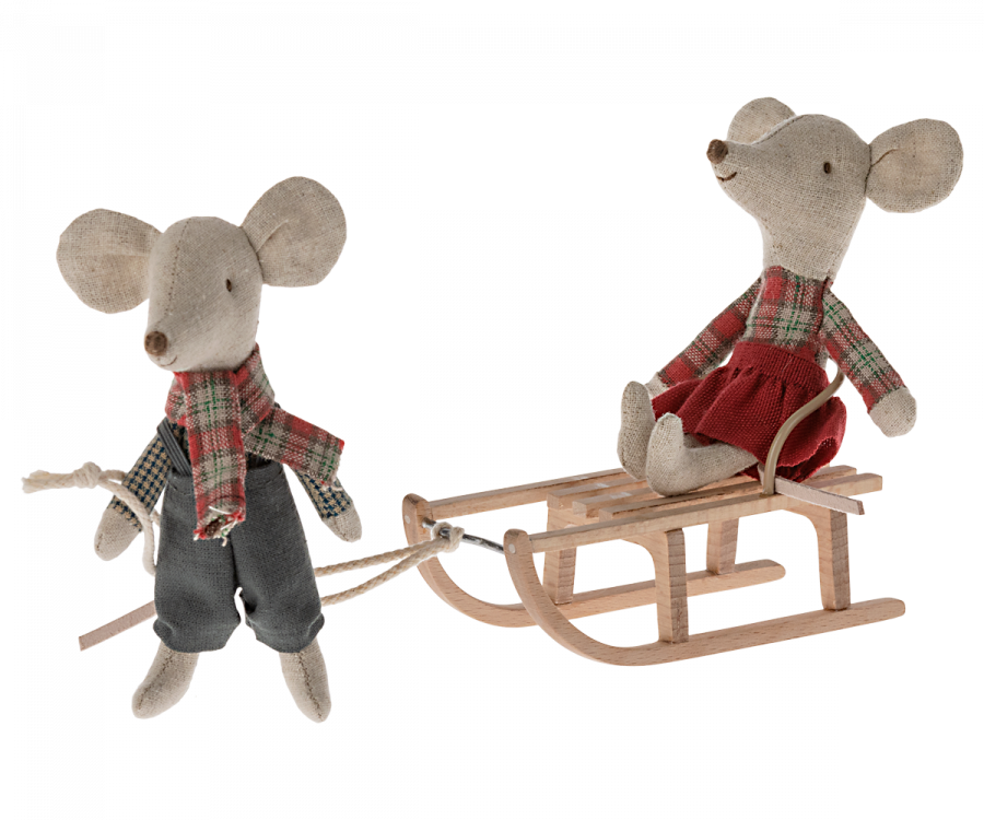 Two fabric mice dolls, both dressed in plaid shirts and scarves, bring winter charm. One mouse, wearing pants, pulls a Maileg Christmas Mini Sled with a rope. The other mouse, in a red skirt, sits on the sled enjoying the ride—a delightful snow toy and winter accessory combined beautifully.