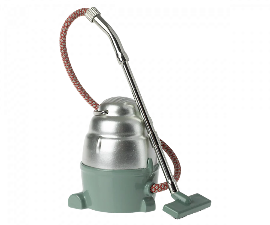 Vintage green and silver Maileg Miniature Vacuum Cleaner with a long hose and a fabric-covered cord, isolated on a grey background.