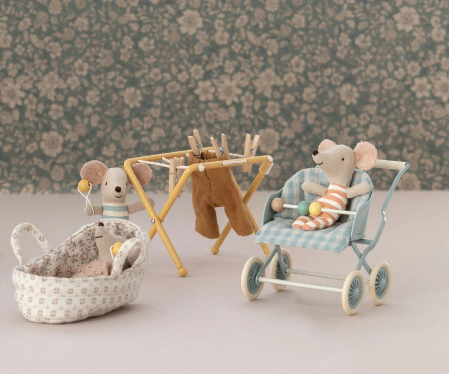 A whimsical scene featuring toy mice in a vintage-style nursery. One mouse sits in a Maileg Stroller, Baby Mice - Mint, another peeks over a drying rack with tiny clothes, and a third sleeps in a small patterned basket. The background has floral wallpaper, adding a nostalgic touch reminiscent of cozy mouse families from storybooks.