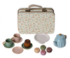 A decorative metal suitcase with a Maileg print is displayed with a Maileg Miniature Afternoon Treat Tea Set - Merle in front. The set includes two cups with saucers, a blue teapot, a bundt cake, a white plate, and four colorful macarons.