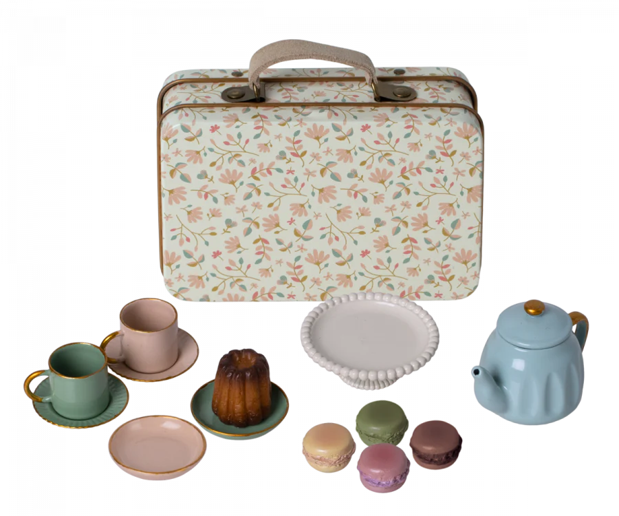 A decorative metal suitcase with a Maileg print is displayed with a Maileg Miniature Afternoon Treat Tea Set - Merle in front. The set includes two cups with saucers, a blue teapot, a bundt cake, a white plate, and four colorful macarons.