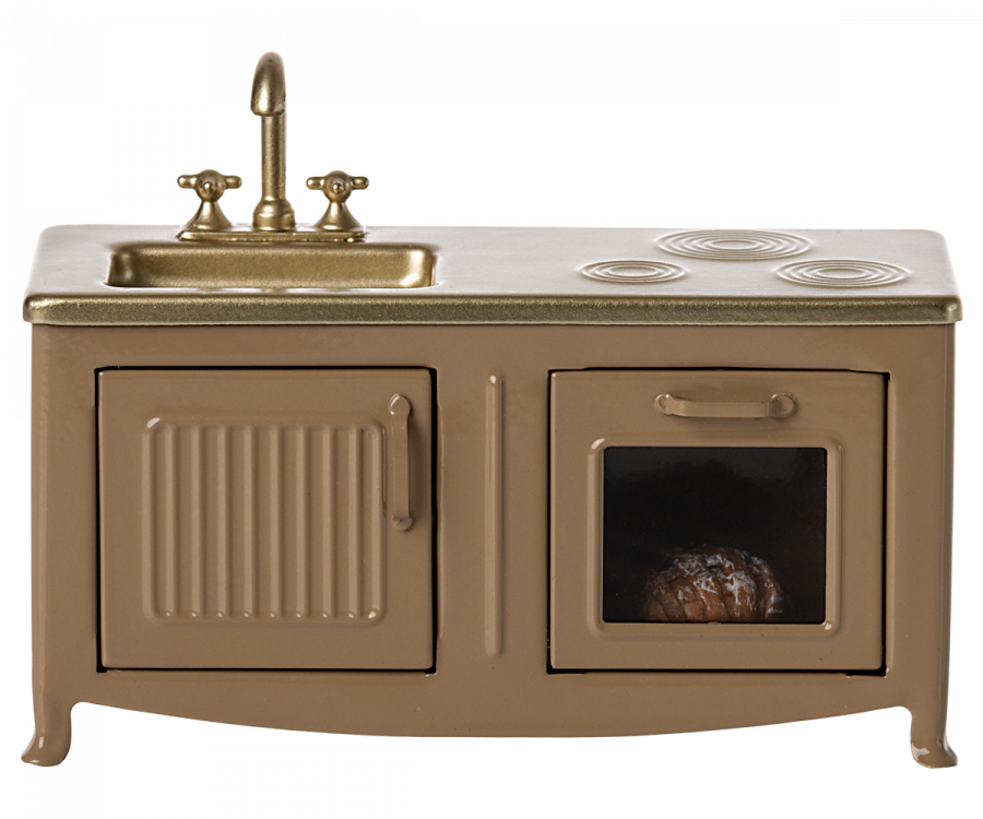 A Maileg Kitchen - Light Brown featuring a beige cabinet with a sink, faucet, and a stove top. One of the cabinet doors is open, revealing a small pie inside.