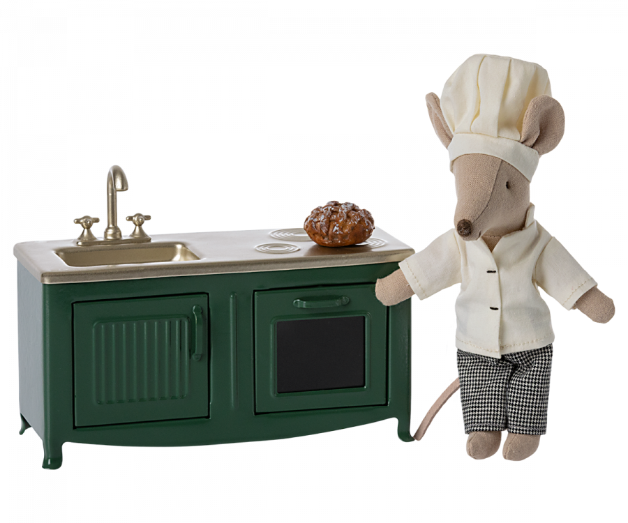 A plush mouse chef in a white chef's hat and jacket stands beside a Maileg Kitchen - Dark Green, holding a small whisk and presenting a freshly baked pie.