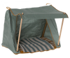 A green canvas Maileg Happy Camper Tent for pets with a cozy striped cushion inside. The tent is supported by thin wooden poles, featuring an open front and a flat top.