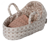 A small, beige, fabric baby bassinet with two handles, decorated with a floral pattern. Inside the bassinet is a pink, knitted blanket, neatly folded—ideal as a charming Maileg Carry Cot, Baby.