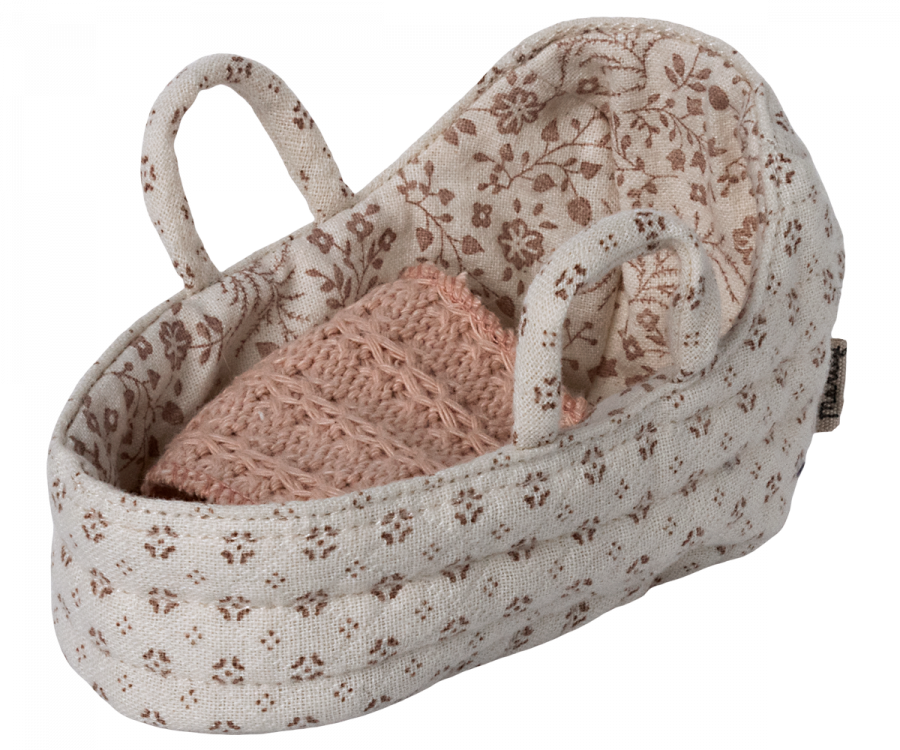 A small, beige, fabric baby bassinet with two handles, decorated with a floral pattern. Inside the bassinet is a pink, knitted blanket, neatly folded—ideal as a charming Maileg Carry Cot, Baby.