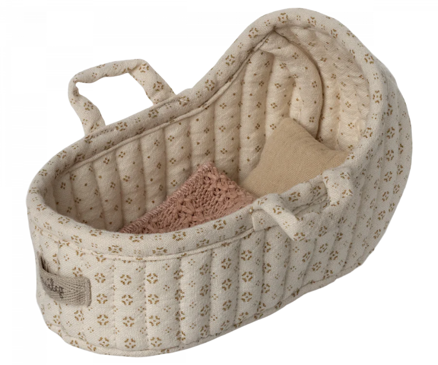 A small, beige, fabric Maileg Carry Cot, Micro with a quilted pattern and floral designs. The cot contains two small pillows, one pink and the other light beige. This versatile piece doubles as a micro-sized bunny bed or portable rabbit carrycot, complete with soft handles for easy carrying.