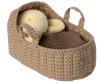 A plush teddy bear nestled inside a large, sand-colored Maileg Carry Cot, adorned with a knitted brown blanket. The carrycot features two convenient handles, making it perfect for cozy travels.