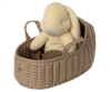 A plush bunny rests inside the Maileg Carry Cot, Large - Sand, featuring a charming quilted texture and convenient handles. The basket's patterned beige design resembles an adorable carrycot, complete with a small tag on the side. The bunny is crafted from a soft, off-white material.