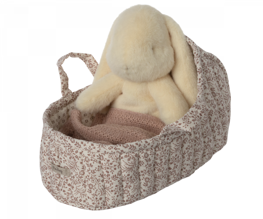 A Maileg Carry Cot, Large - Off White, cradles a plush rabbit toy in cozy floral-patterned fabric, complete with a warm knitted blanket. The carrycot features a convenient small handle and is complemented by the pastel-colored rabbit for an adorable and snug on-the-go companion.