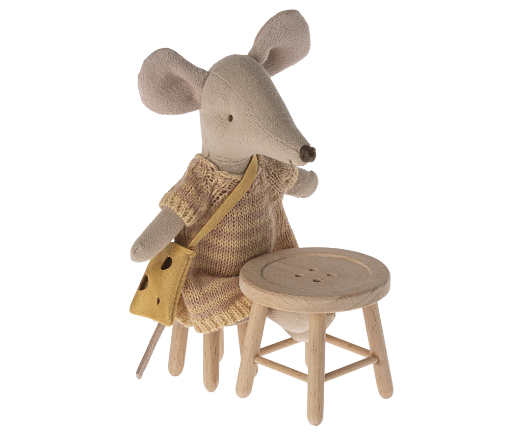 A plush toy mouse wears a yellow knitted dress and matching satchel. It stands next to the Maileg Table & Stool Set, Mouse, perfectly suited for any mouse hole farmhouse. With large, round ears and a long snout, this whimsical character brings joy to the scene.