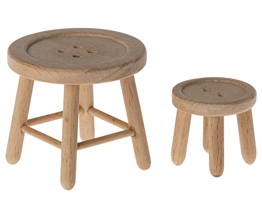 Two small wooden stools with button-patterned tops evoke the charm of farmhouse decor. The larger stool, part of a Maileg Table & Stool Set, Mouse, has a round seat with four legs joined by crossbars for support, while the smaller three-legged stool could easily belong in a mouse family furniture collection. Both feature smooth, unfinished surfaces.