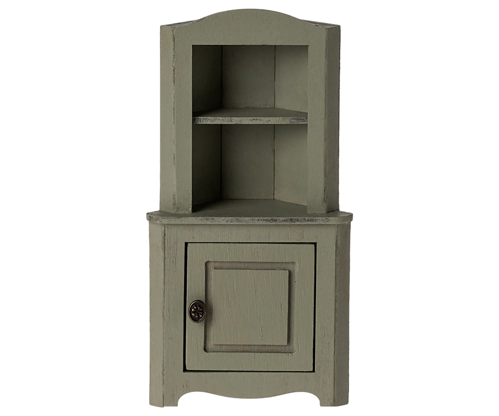 The Maileg Corner Cabinet, Mouse - Light Green is a small, rustic wooden corner cabinet with a vintage finish. It features an open shelf area at the top with two compartments and a closed compartment at the bottom with a single door and round metal knob. Perfect for home decoration.