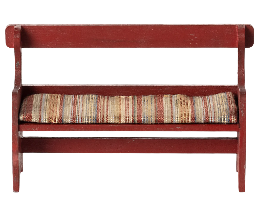 The Maileg Mouse Bench - Red, available in approximately one week, is a compact wooden piece with a vintage aesthetic, featuring a red finish and a woven seat cushion with multicolored stripes. Its straightforward design includes both backrest and armrests, ideal for adding nostalgic charm to any room.