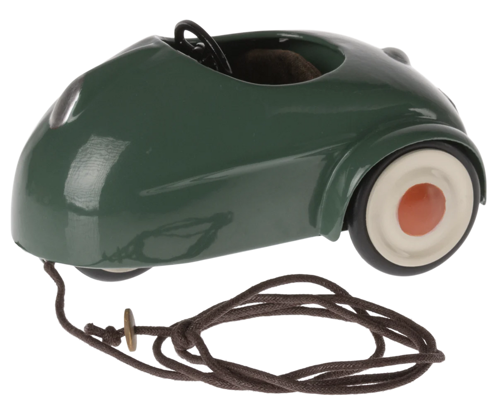 An image of a Maileg Mouse Car - Dark Green, metal car with a shiny finish. It features a simple white and red wheel design on the front with a visible brown cord attached.