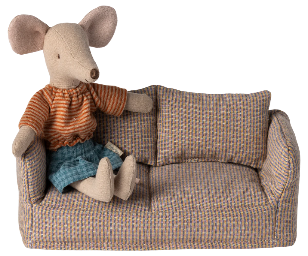 A fabric mouse doll, styled for children, wearing an orange striped shirt and blue skirt rests on a plush Maileg Mouse Couch. The petite couch features a plaid pattern with two cushions, exuding a handmade appeal that captures the Mouse Hole Farmhouse charm.