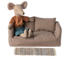 A stuffed mouse toy wearing a striped orange shirt and blue shorts is seated on a plaid-patterned mini sofa with matching cushions. Enhancing the cozy atmosphere, the scene features the Maileg Striped Rug, Large positioned in front of the sofa.