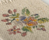 Close-up of the Maileg Flower Rug in a small size, showcasing its intricate cross-stitched floral design with reds, yellows, purples, and greens. The neutral beige background beautifully highlights these vibrant stitches, enhancing charm in any setting. Please note it ships in approximately one week.