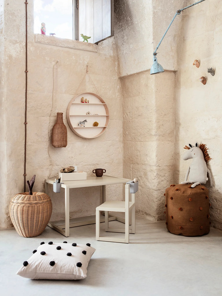 A cozy minimalist corner featuring a small desk with a mug and book, round shelving on the wall, comfortable floor cushions, and Hand Carved Animal Wall Hooks in a room with textured stone walls and a large