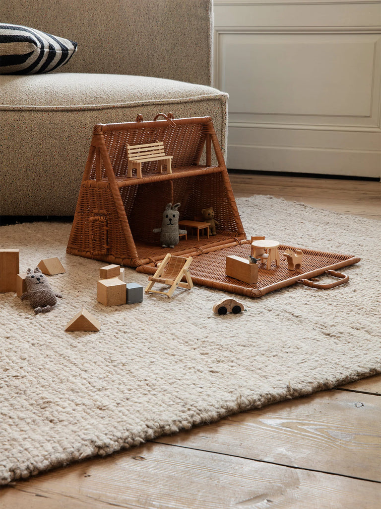 A cozy children's play area with a Braided A-Frame Dollhouse, tiny furniture, and plush toys on a soft, white rug, depicting a serene indoor play setup.