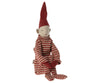 A Maileg Long Legged Pixy, featuring a red pointed hat and a red and white striped knitted suit. The doll has a simple stitched face and long limbs, sitting with its legs extended and arms crossed. It exudes a whimsical and festive charm.