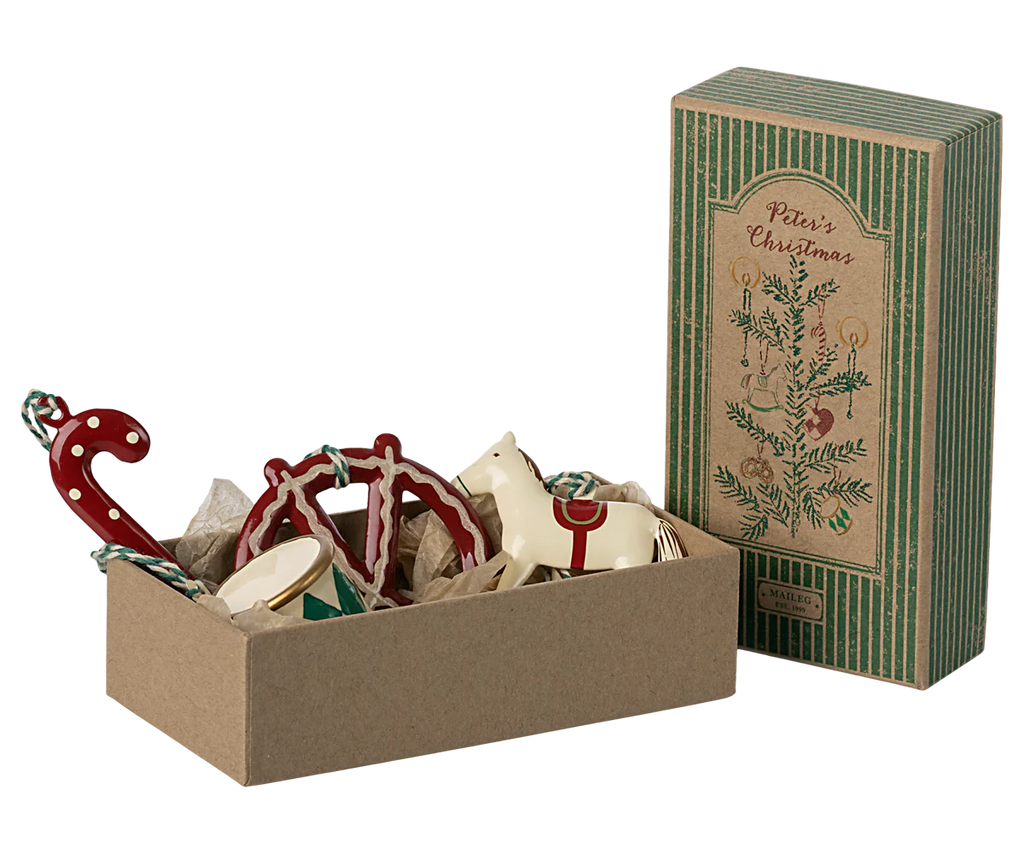 The Maileg Peter's Christmas Ornament Set (2024) features an attractive cardboard gift box adorned with charming ornaments such as a candy cane, horse, drum, and heart shapes. The box is lined with paper and is accompanied by a matching upright rectangular package.