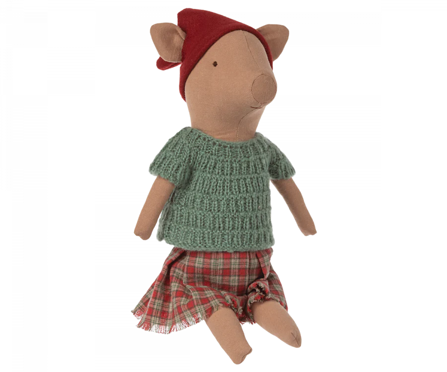 The Maileg Christmas Pig - Girl is a cozy plush piglet, dressed in a festive red hat, green knitted sweater, and red plaid skirt, sitting upright and perfect for the holiday season.