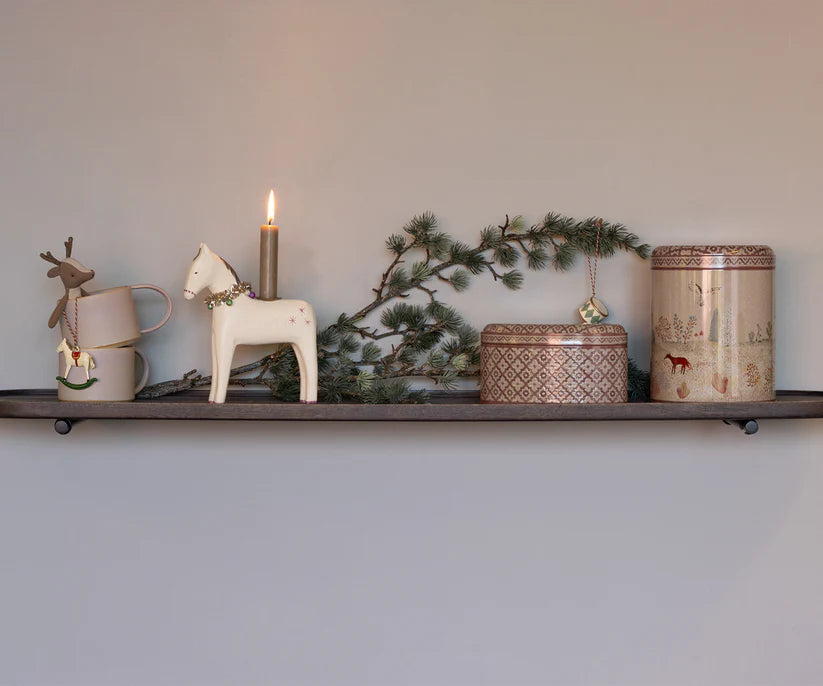 The shelf features a mug, a reindeer decoration, a white horse figurine with a lit candle, pine branches, and two tins from the Maileg Metal Box 2 Piece Set - Winter Wonderland collection. This festive display combines natural and Scandinavian-inspired elements for a cozy atmosphere.