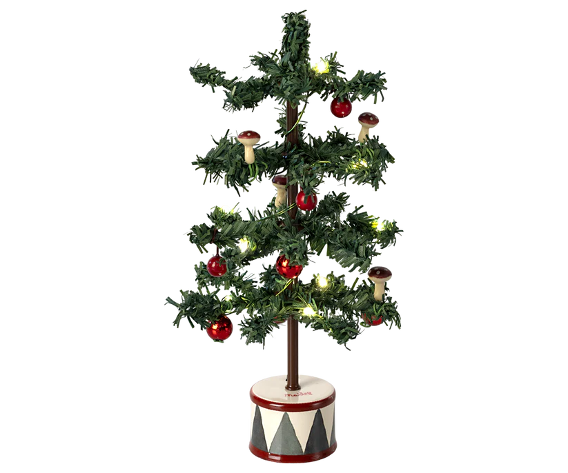 The Maileg Christmas Tree, Mouse is a compact artificial Christmas tree with sparse green branches decorated with red and brown mushrooms. It includes glowing LED bulbs and stands on a round, white and red base adorned with a geometric pattern, evoking the charm of a gingerbread house.