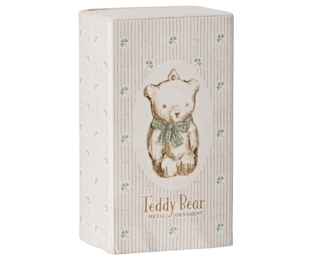 A decorative box showcases a vintage-style illustration of a teddy bear with a green bow, accentuated by hand-painted details. The box is adorned with a subtle striped pattern and small clover-like motifs, featuring the text "Maileg Metal Ornament, Teddy Bear - Off White/Blue" at the bottom, reminiscent of charming Maileg ornaments.