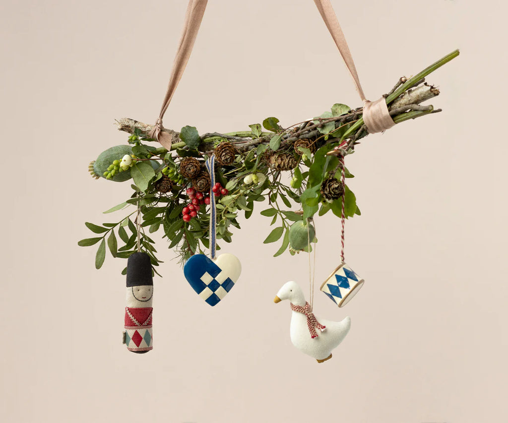 A handmade Christmas tree decoration showcasing a collection of greenery and pinecones adorned with four Maileg ornaments, including the Maileg Guard Ornament in red, a heart, a duck, and a small round design. Each ornament is crafted in festive colors.