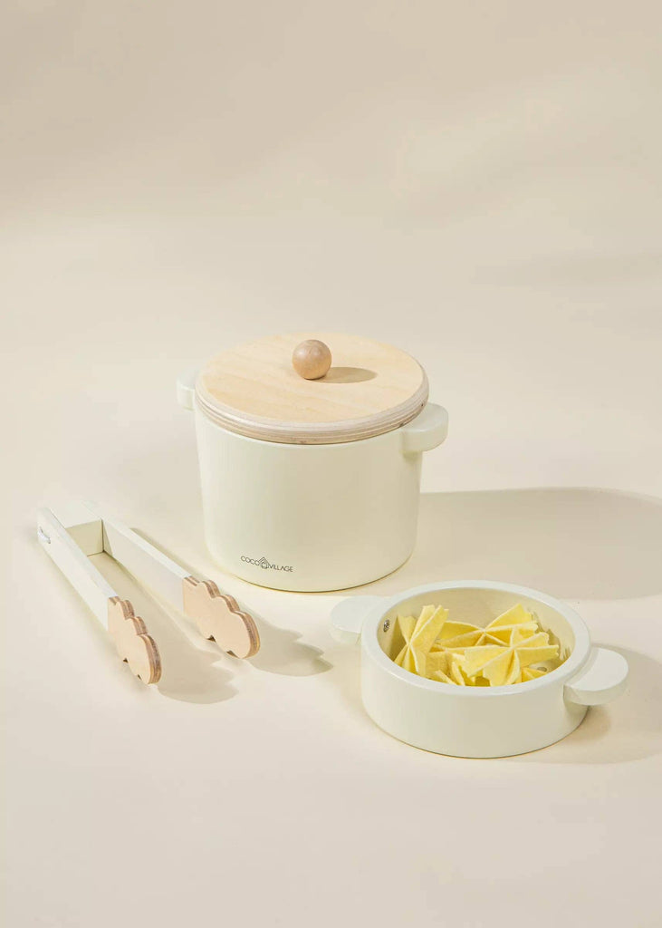 The Wooden Pasta Playset sparks creativity in children, showcasing a cream-colored saucepan with a wooden lid, wooden-handled tongs, and a coordinating bowl brimming with uncooked pasta. It's ideal for imaginative play against a light backdrop.