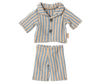 The Maileg Extra Clothing: Pyjamas for Teddy Junior include a stylish short-sleeved collared shirt with buttons and matching pants, featuring vertical blue and beige stripes. Each piece can be purchased separately.