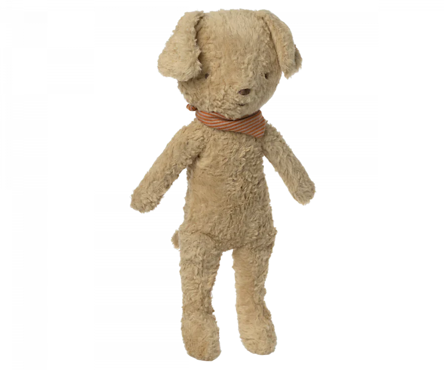 An old, well-loved Maileg plush dog with a worn-out beige fur and a vintage dog-striped orange and green bow tie, standing upright against a black background.