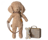 A Maileg Puppy Accessories - Rose with floppy ears stands upright, attached to a collar and leash. Beside the toy is a small metal suitcase and a white plush bone decorated with a floral pattern.