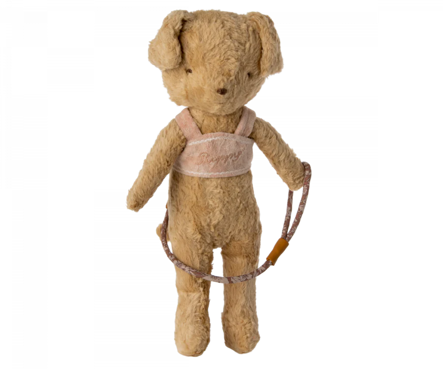 A vintage-style teddy bear dressed in a cozy beige harness with "Benny" embroidered in cursive. The bear is holding a patterned leash in its left paw and stands upright against a plain white background. The fur is light brown, and the Maileg Puppy Supply, Harness exudes a nostalgic charm, reminiscent of beloved puppy supplies.