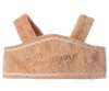 A soft, pinkish-beige Maileg Puppy Supply, Harness with "Puppy" embroidered on it in cursive beige thread. The velvety harness features decorative white stitching along the edges and two padded shoulder straps.