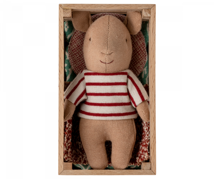 A Maileg Pig In Box, Baby - Girl, wearing a red and white striped shirt, lies inside a rectangular wooden box. The box is lined with a patterned fabric resembling a small blanket and pillow. The playset features the pig's simple, smiling face, with its head slightly turned to the right.