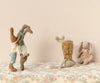 Four Maileg Bunnies, Size 2 - Flower Dress are displayed, each made of recycled polyester and wearing soft natural fabrics. Two bunnies are standing on their hands, supported by another bunny. Another bunny is sitting in a floral dress. They are placed against a soft-colored background and a floral tablecloth.